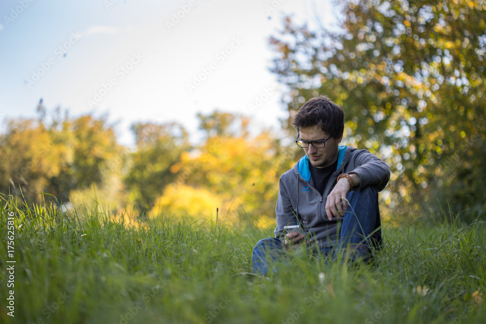 Junger Mann sitzt im Gras, Blick aufs Smartphone, Textfreiraum Junger Mann sitzt im Gras, Blick aufs Smartphone, Textfreiraum