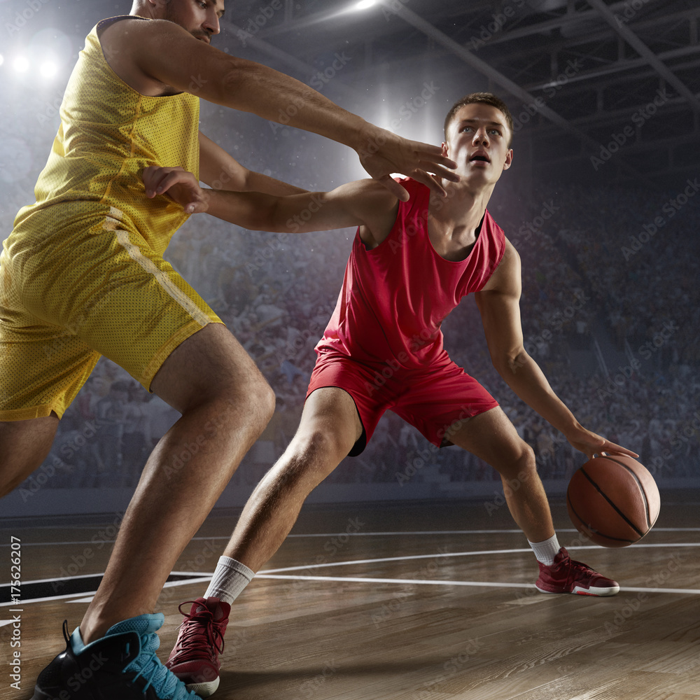 Two basketball players fight for the basketball ball on big professional arena. Player wears unbranded clothes.