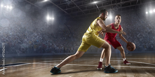 Two basketball players fight for the basketball ball on big professional arena. Player wears unbranded clothes. © Alex