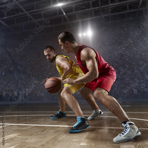 Two basketball players fight for the basketball ball on big professional arena. Player wears unbranded clothes. © Alex