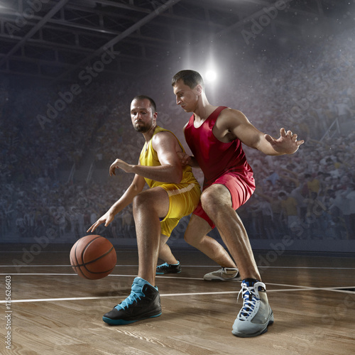 Two basketball players fight for the basketball ball on big professional arena. Player wears unbranded clothes.