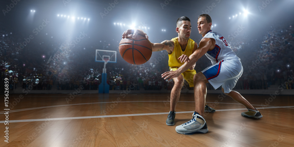 Two basketball players fight for the basketball ball on big professional arena. Player wears unbranded clothes.