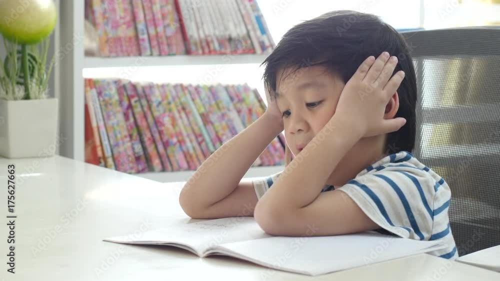 Unhappy Asian child working on hard homework at home alone Unhappy Asian child working on hard homework at home alone