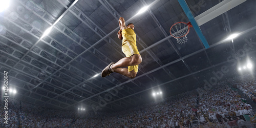 Basketball player makes slam dunk on big professional arena. Player flies through the air with the ball. Player wears unbranded clothes. Bottom view.