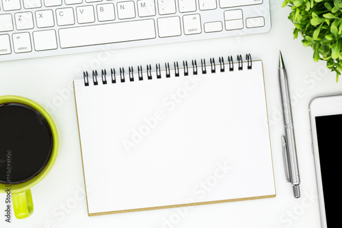 White office desk table with blank notebook page and supplies. Top view  flat lay.