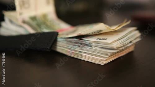 A bundle of banknotes, tied with a money red rubber band, lying on a dark wooden table, close-up