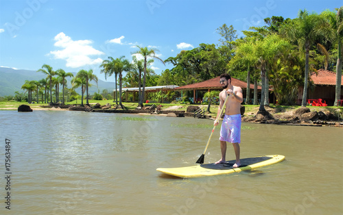 Homem jovem praticando paddleboarding, stand up paddle, remando. Surfando com remo. fundo com praia e palmeiras.