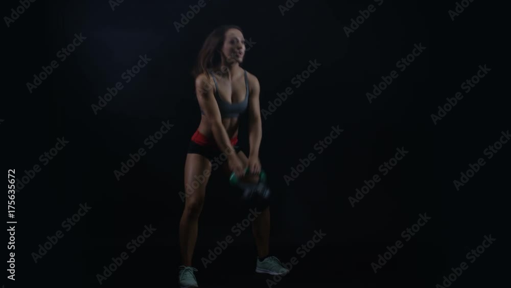 Fit young woman working out with kettle bell weight against black background Fit young woman working out with kettle bell weight against black background