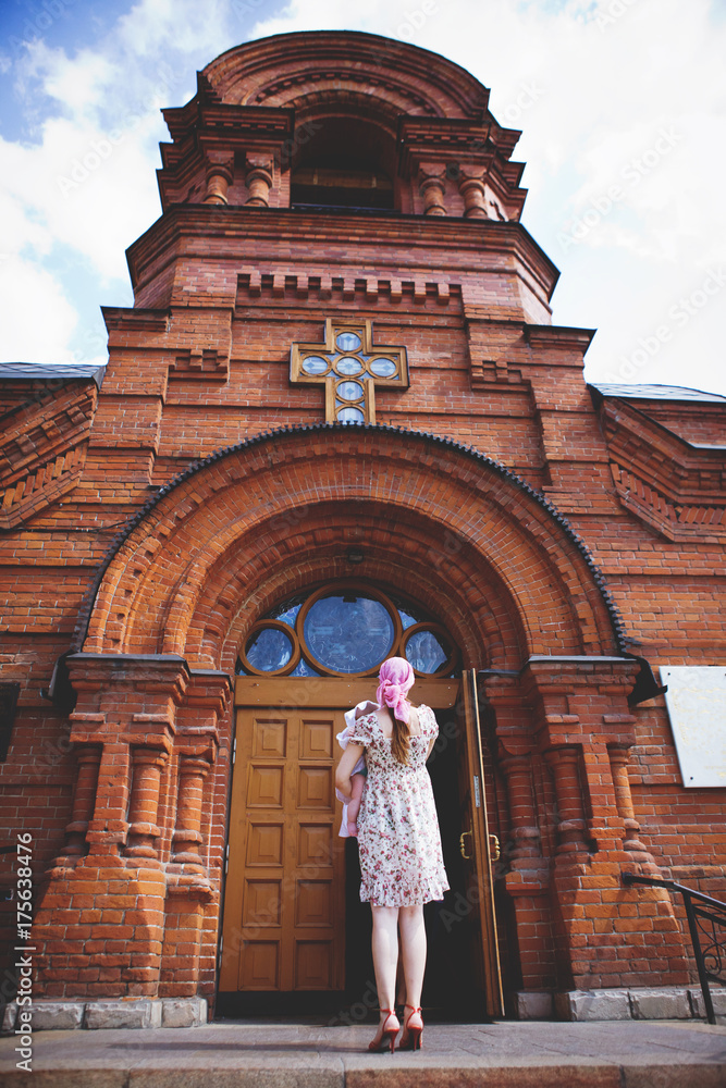 A woman holding a child in her arms, at the entrance to the Orthodox Church.