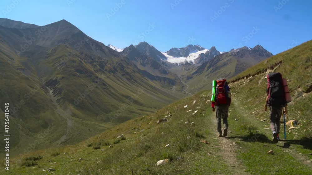Two friends are hiking by the road in the mountains. Friends are walking in mountains 4K UHD Two friends are hiking by the road in the mountains. Friends are walking in mountains 4K UHD