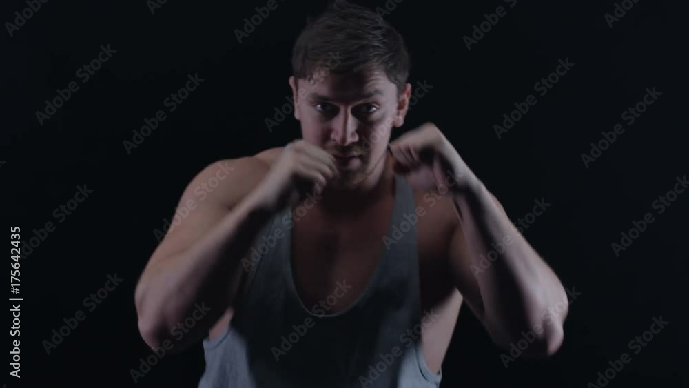 Muscular boxer training, throwing punches towards camera with bare fists Muscular boxer training, throwing punches towards camera with bare fists