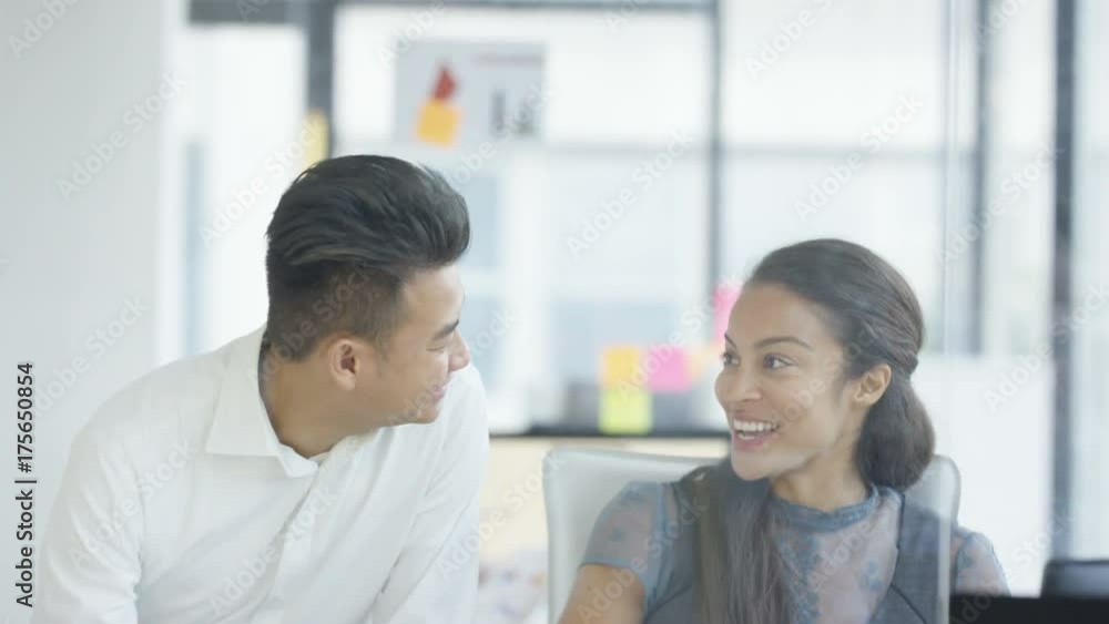 Businesswoman working on computer at her desk & talking to a colleague Businesswoman working on computer at her desk & talking to a colleague