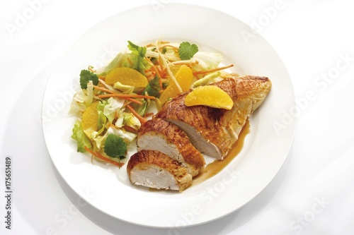 Roasted chicken breast garnished with orange segments served on a plate with a mixed salad