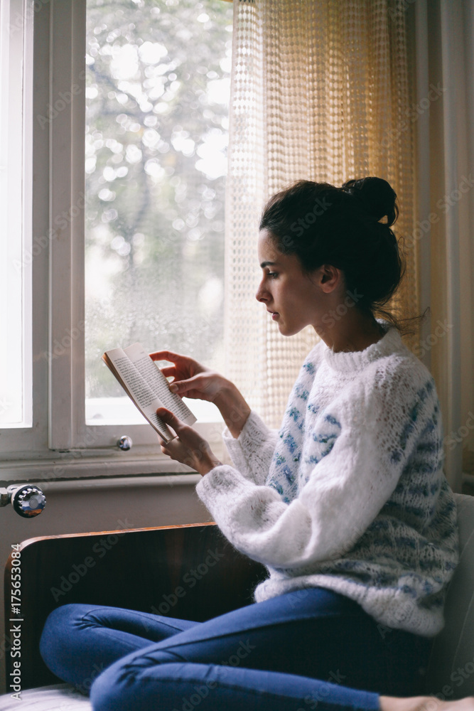 Beautiful woman reading a book in her room near the window Beautiful woman reading a book in her room near the window