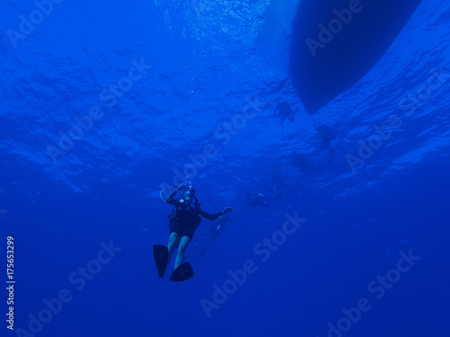 Diver Descending into the Blue Ocean below Boat Silhouette on Surface