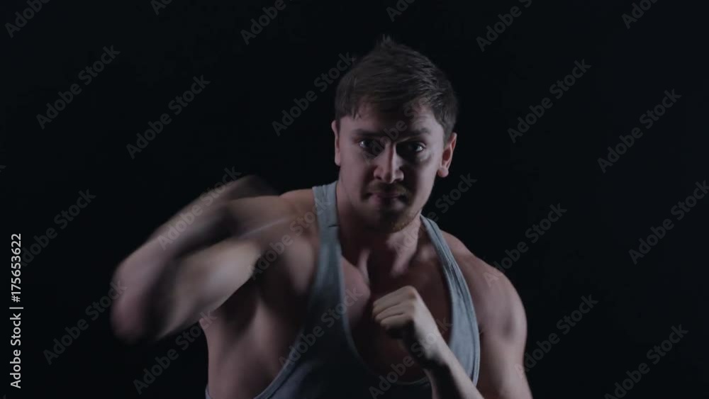 Muscular boxer training, throwing punches towards camera with bare fists Muscular boxer training, throwing punches towards camera with bare fists