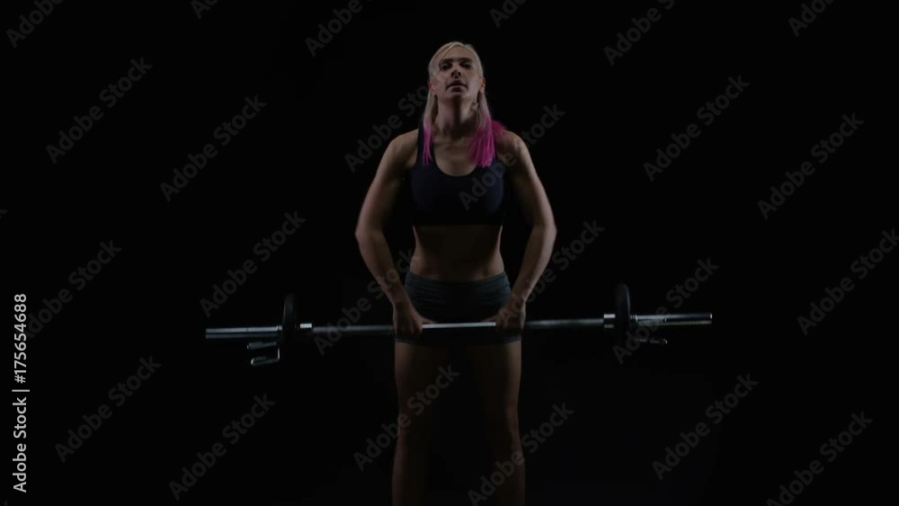 Fit woman with athletic physique lifting weights against black background Fit woman with athletic physique lifting weights against black background