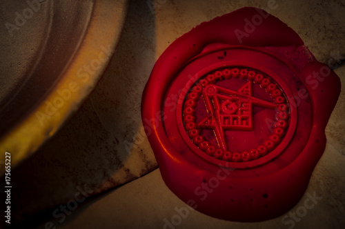 Freemason secret symbol concept with vintage letter under a candle, sealed with red wax seal with the square, the compass and the G letter in the middle, one of the most identifiable masonic symbols photo