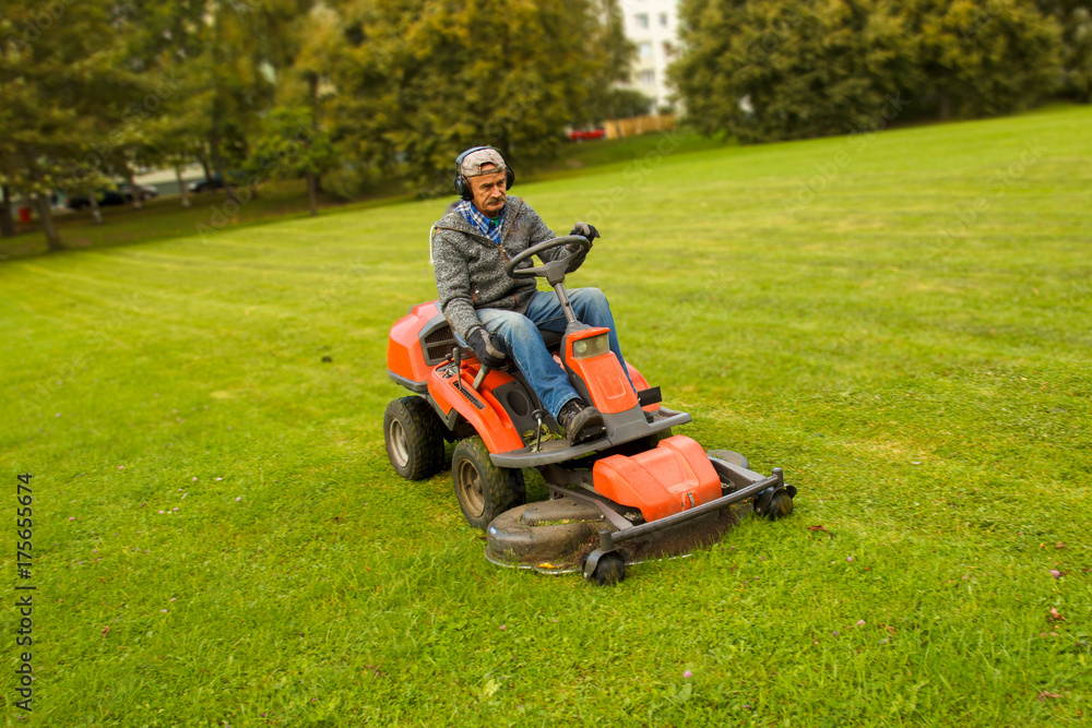 a man driving a lawn mower in a city park a man driving a lawn mower in a city park