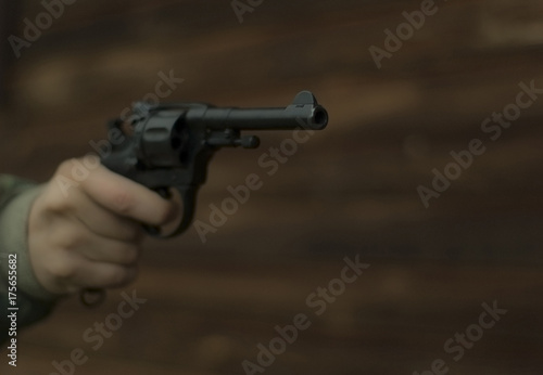 A revolver with a cocked trigger in hand is aiming past the frame against the background of a blurred log wall. Focus on the muzzle, the rest is blurry. photo