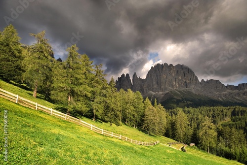 Thunderclouds forming over the peak of Mt. Rosengarten, sunlight shining over a fenced alpine pasture, San Zyprian, Bolzano-Bozen, Italy, Europe photo