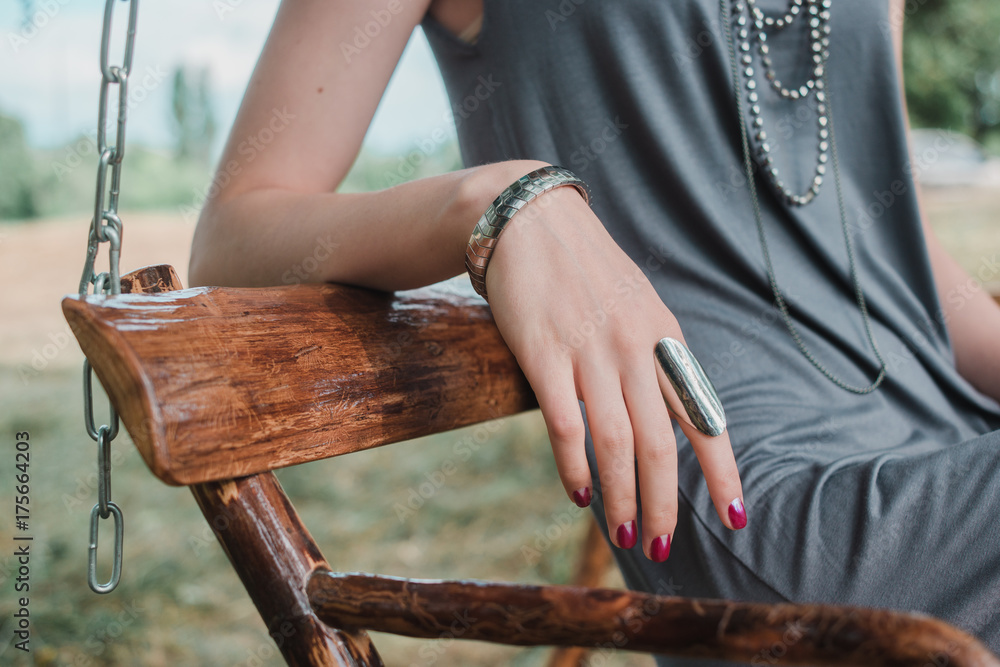 Young beautiful girl sits in a park on a wooden swing made of eco-friendly materials, resting on the day off. Close up of her hand with rings and bracelet