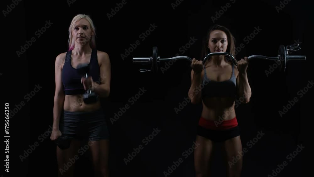 2 Fit young women working out with weights against a black background 2 Fit young women working out with weights against a black background