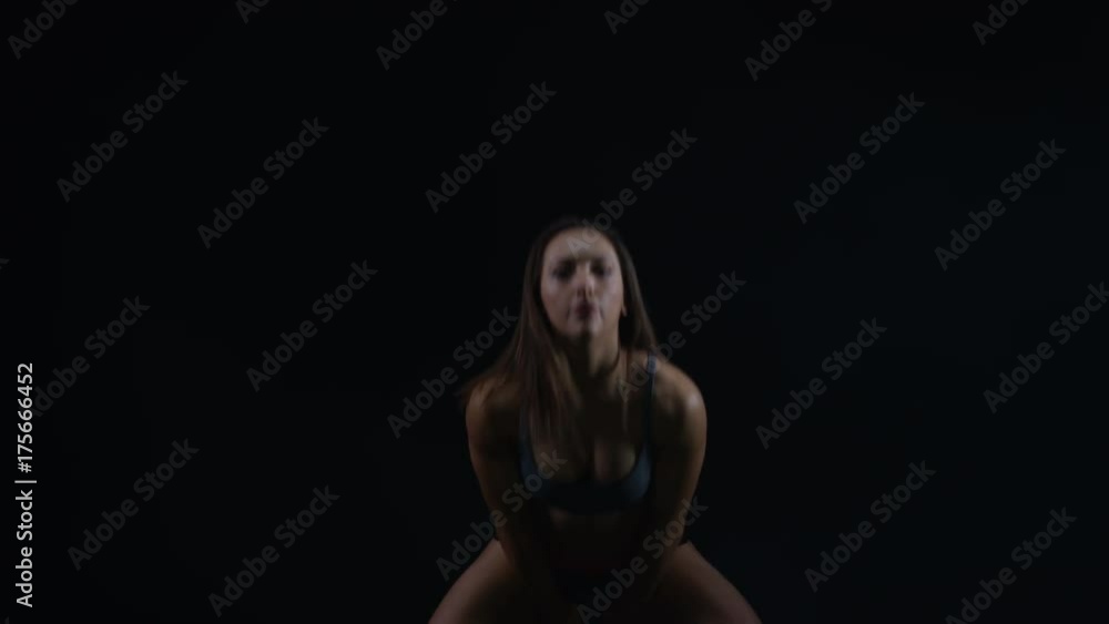 Fit young woman working out with kettle bell weight against black background Fit young woman working out with kettle bell weight against black background