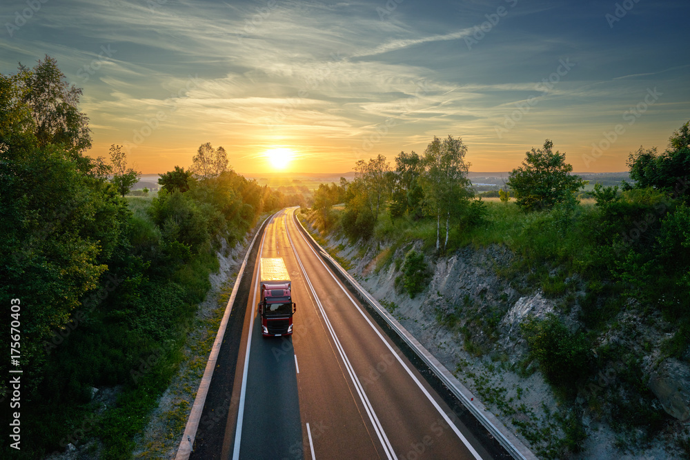 Truck driving on the highway in a rural landscape at sunset. View from above.
