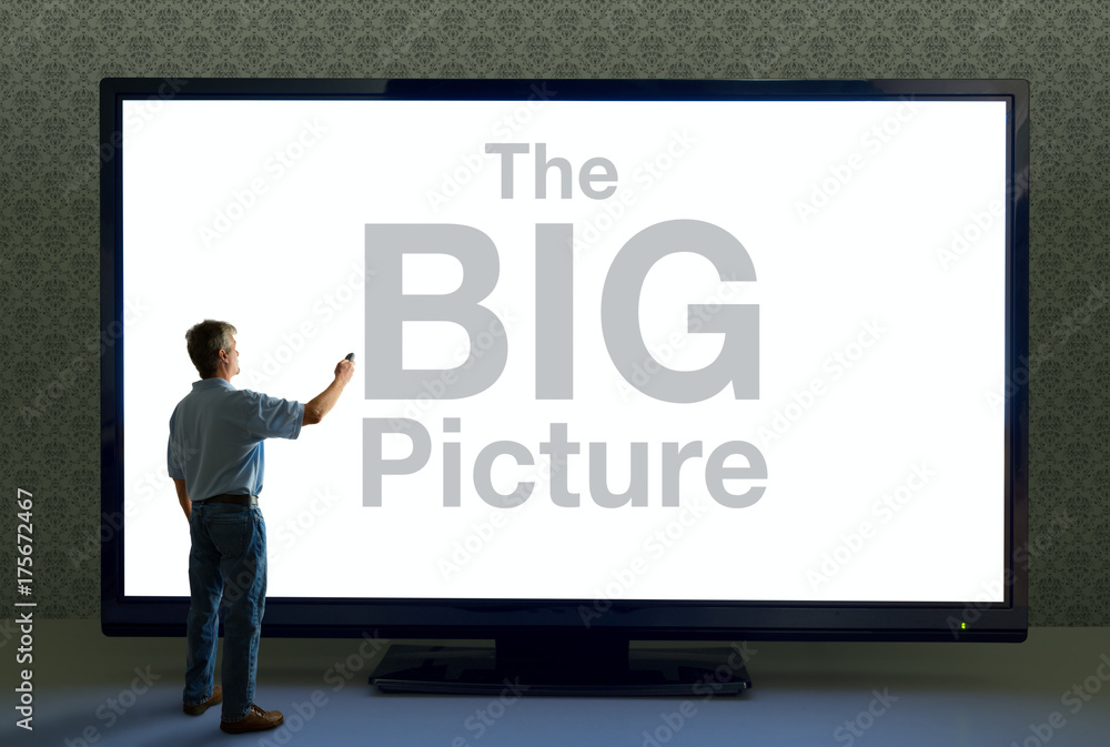 Man pointing a remote at a giant TV television that saying The BIG Picture  in huge text representing importance, good deals, story details, digital  overload, technology advancements and more. Stock Photo