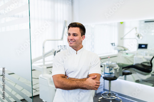 Portrait of handsome smiling dentist standing with his hands crossed in his stomatology office.