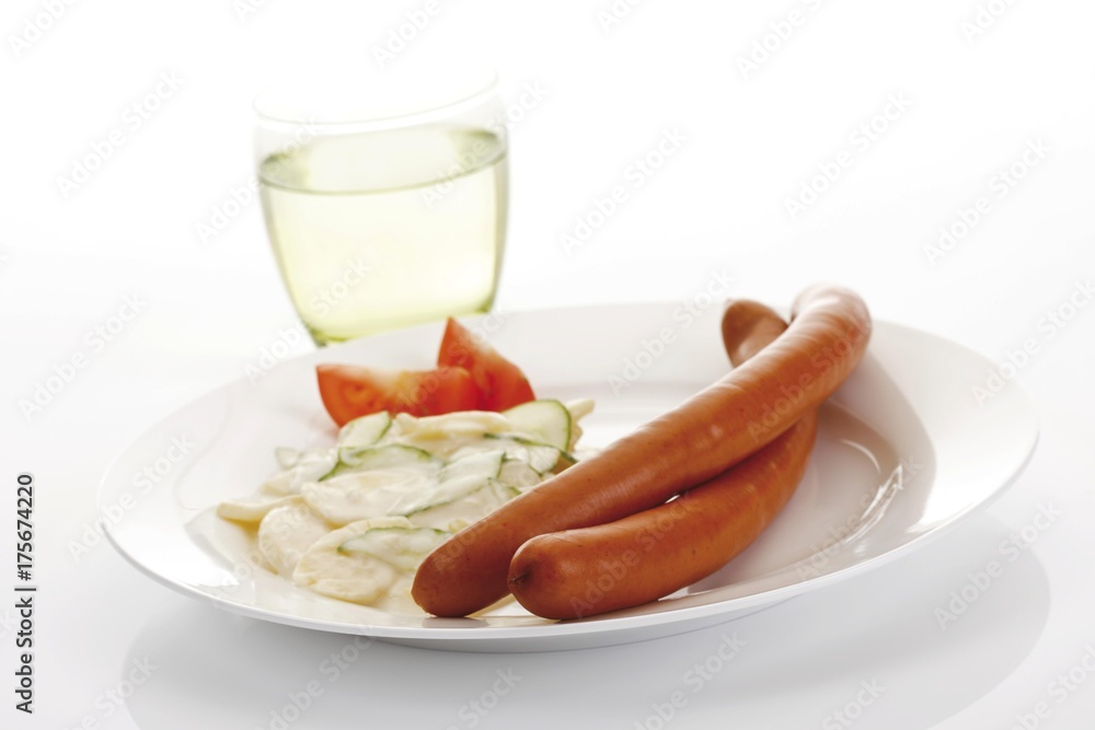 Sausages with potato salad on a plate and a glass of mineral water Sausages with potato salad on a plate and a glass of mineral water