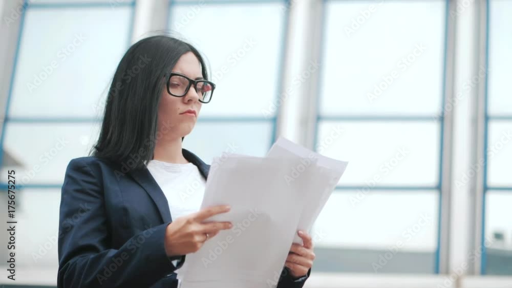 A young beautiful brunette woman in suit and glasses checks documents, utility bills. Slow motion. Businesswoman standing near office. A young beautiful brunette woman in suit and glasses checks documents, utility bills. Slow motion. Businesswoman standing near office.