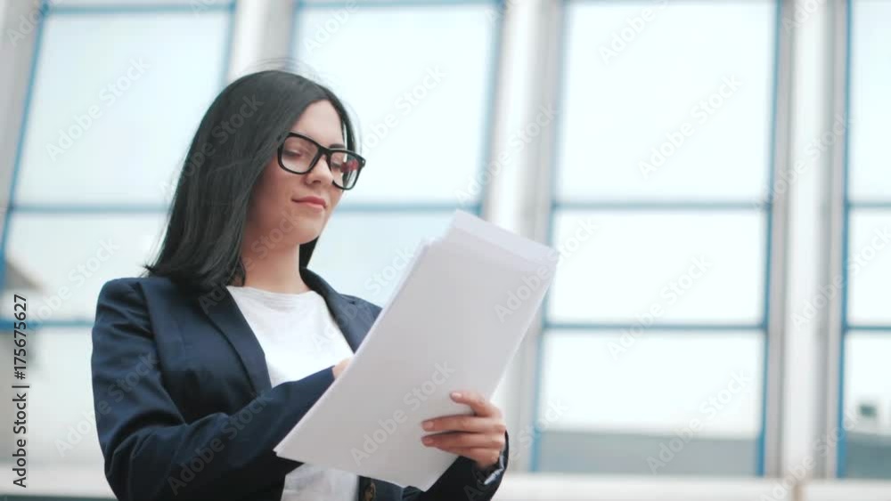 A young beautiful brunette woman in suit and glasses checks documents, utility bills. Slow motion. Businesswoman standing near office. A young beautiful brunette woman in suit and glasses checks documents, utility bills. Slow motion. Businesswoman standing near office.