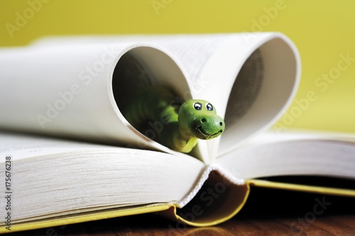 Opened book, bookworm peeking out from pages shaped to form a heart photo