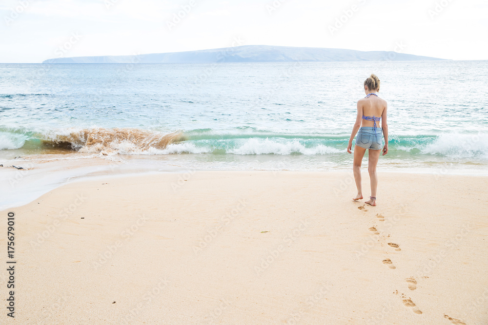 Teenage girl walking alone towards tropical island ocean on beach