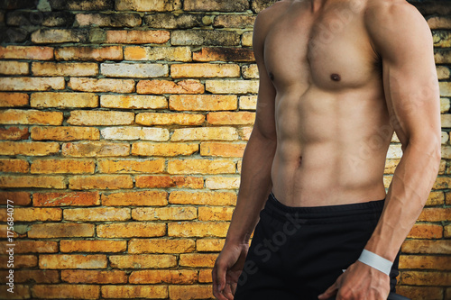 Muscular bodybuilder guy doing posing over brick wall background