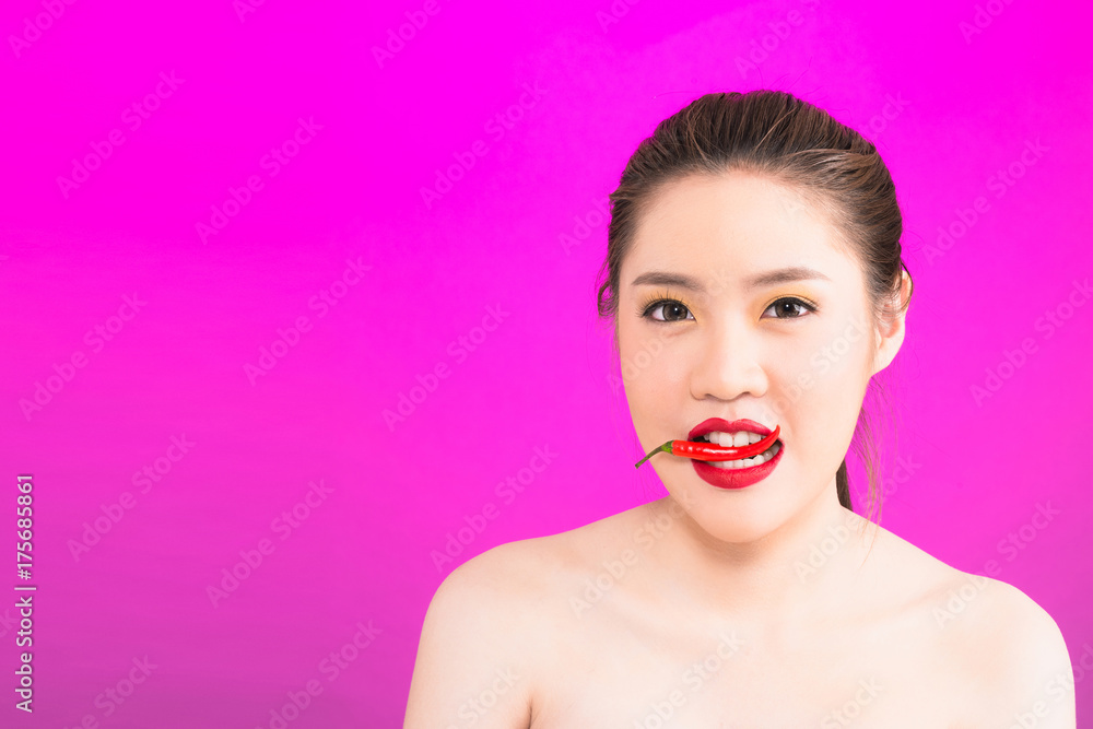 Young Asian woman biting chili isolated in pink background. Young Asian woman biting chili isolated in pink background.