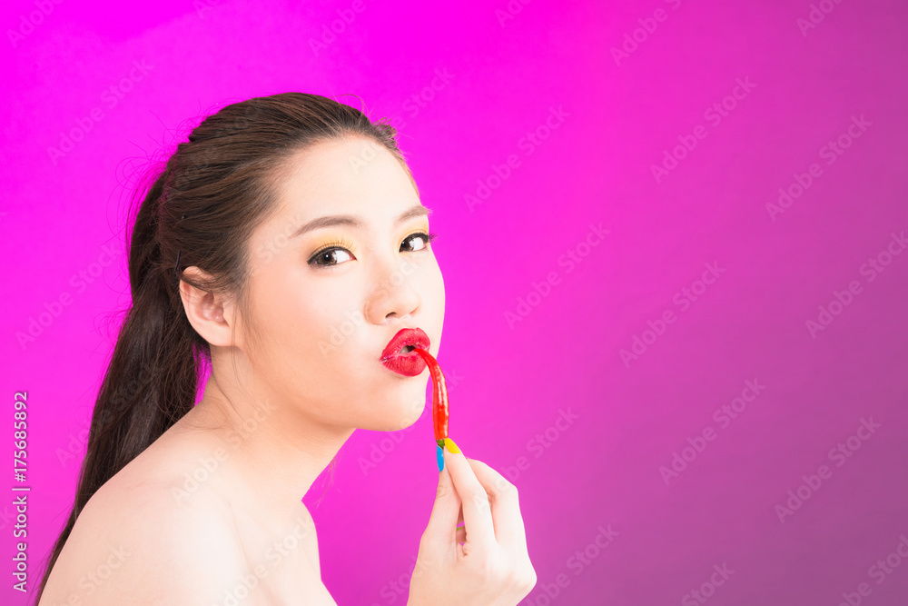 Young Asian woman kissing chili isolated in pink background. Young Asian woman kissing chili isolated in pink background.