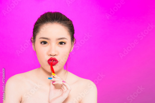Young Asian woman kissing chili isolated in pink background.