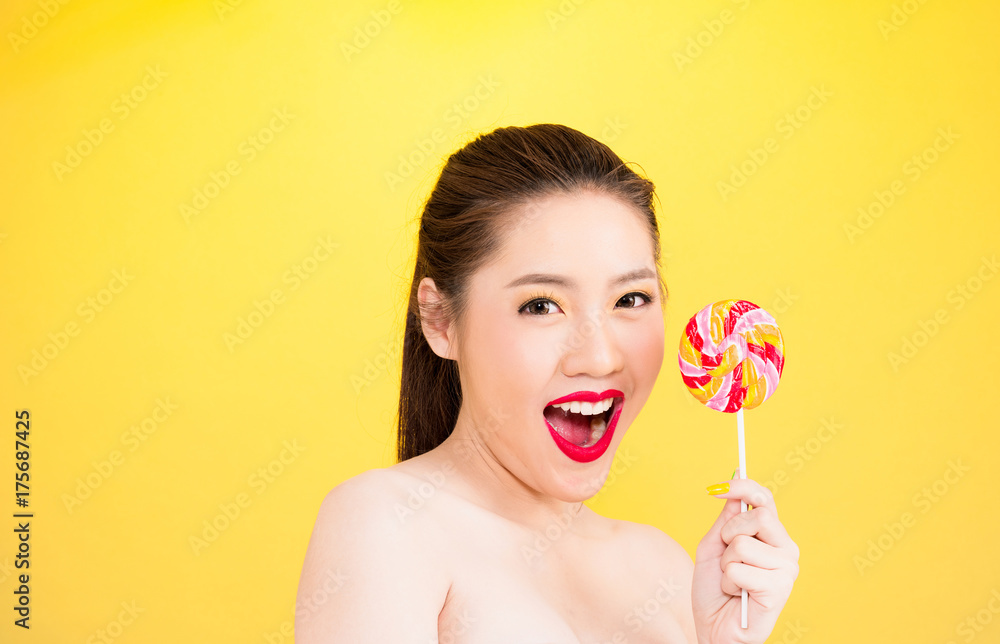 Young Asian woman holding lollipop isolated on yellow background. Young Asian woman holding lollipop isolated on yellow background.