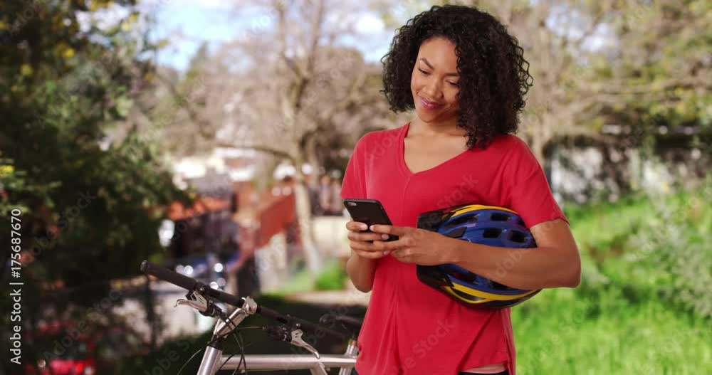 Cute African woman taking break from bicycle ride texting friend on cell phone Cute African woman taking break from bicycle ride texting friend on cell phone