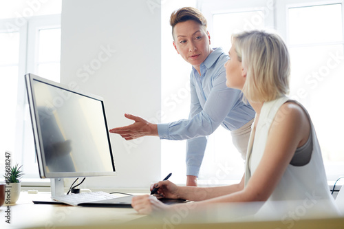 Two modern creative designers or retouchers discussing photos in computer