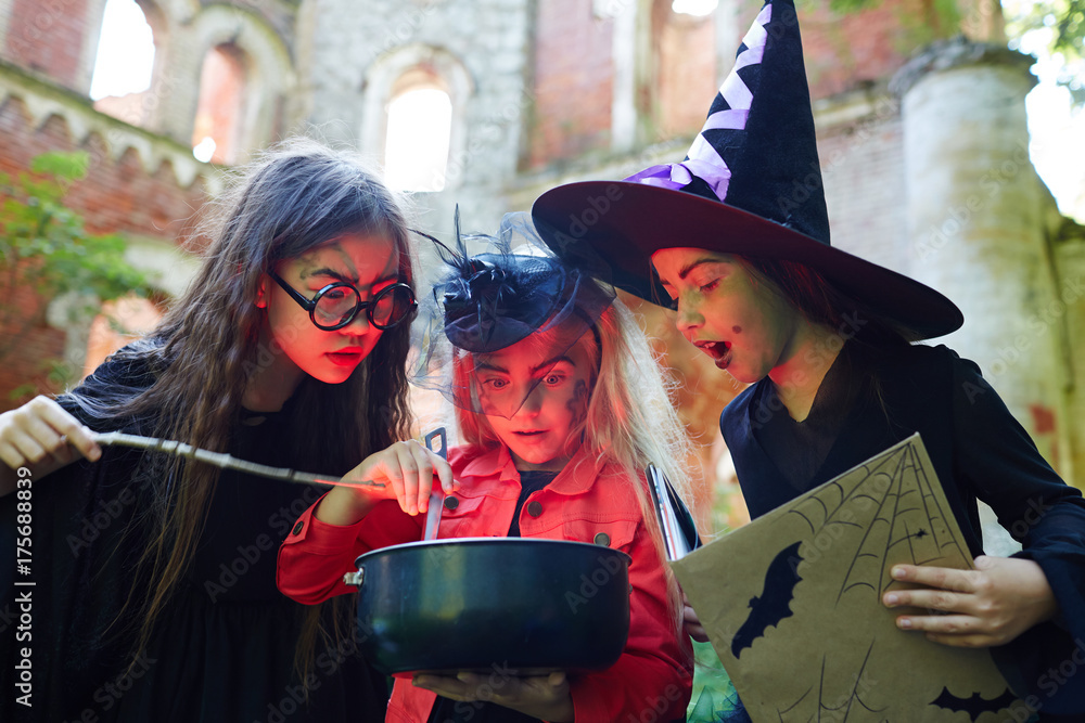 Fototapeta premium Astonished halloween girls looking into pot with witch-brew