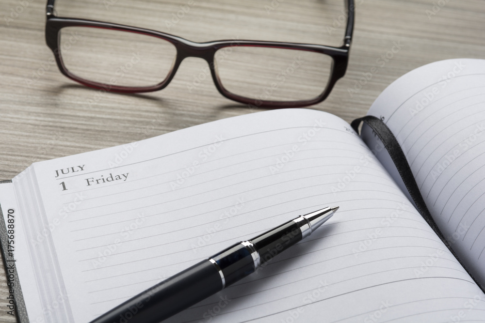 Metal ballpoint pen on a diary and eyeglasses Metal ballpoint pen on a diary and eyeglasses