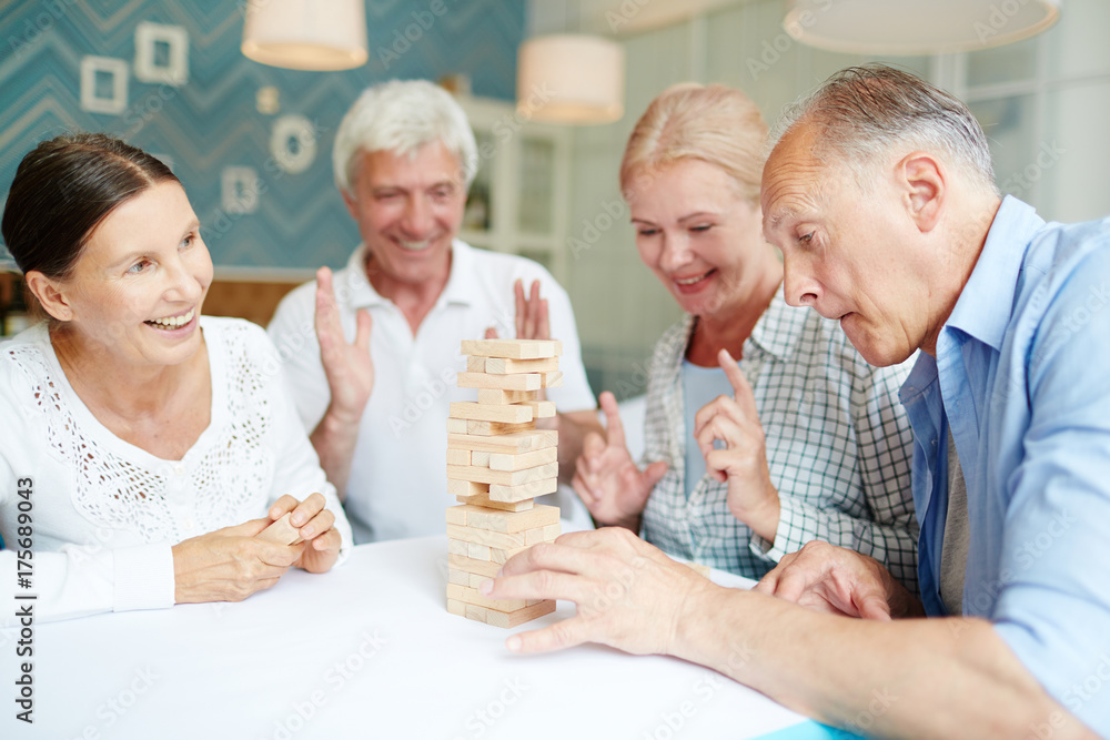 Enthusiastic senior friends playing broad game while spending peaceful evening at cozy living room with stylish design Enthusiastic senior friends playing broad game while spending peaceful evening at cozy living room with stylish design