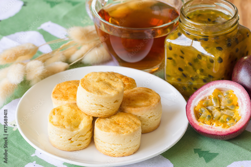 Homemade plain scones serve with homemade passion fruit jam. Scones is traditional English pastry for afternoon tea or coffee break. Delicious plain scones ready to served on wood table.