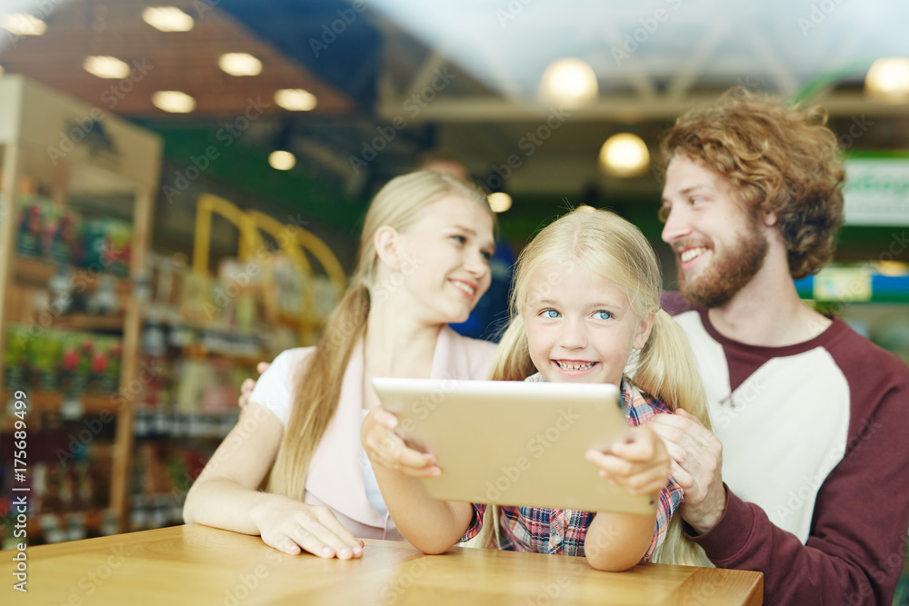 Curious child with touchpad watching video with her parents near by Curious child with touchpad watching video with her parents near by