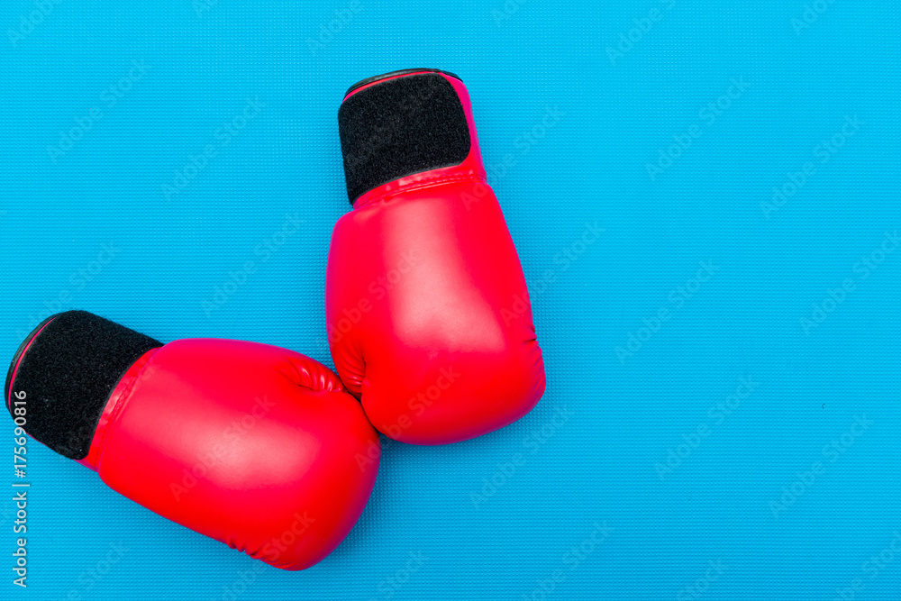 Fitness background with red boxing gloves on blue mat topdown view.