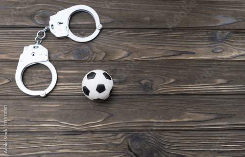 Handcuffs, soccer ball on a wooden background. unlawful actions of football fans photo